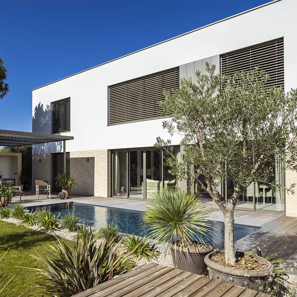 Façade de maison neuve en brique et enduit blanc avec piscine et terrasse bois